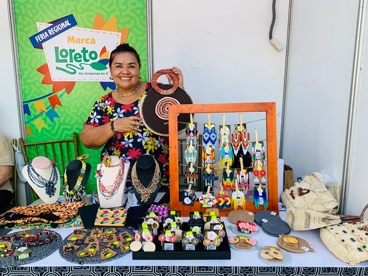 Emprendedora local presentando artesanías hechas a mano, incluyendo tejidos, accesorios y piezas decorativas, exhibidas en un stand.