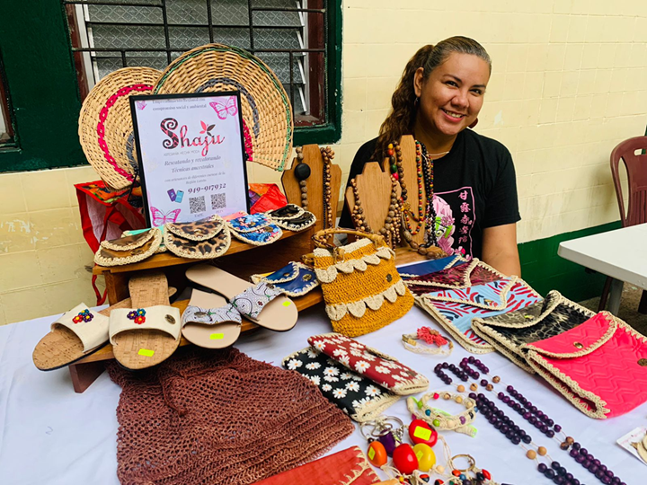 Emprendedora exhibiendo joyería artesanal, textiles y accesorios hechos a mano organizados sobre una mesa.